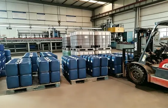 宽敞的化工原料成品仓库内，托盘整齐码放着蓝色塑料桶与大型吨桶，一旁停放着叉车，后方可见生产线设备，阻垢剂主要应用于循环冷却水、锅炉水处理、反渗透膜、油田注水、海水淡化及工业清洗等行业。